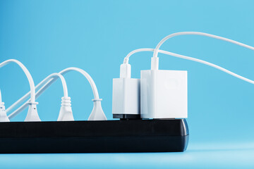 A black mains filter with electrical outlets inserted into it with white plugs of electrical appliances on a blue background