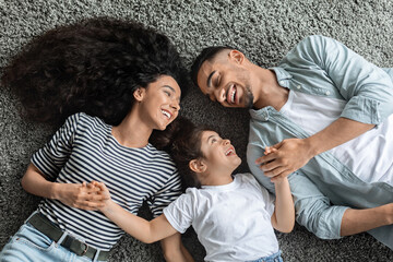 Joyful arabic family laying on floor and holding hands