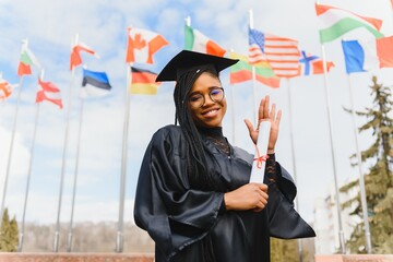 pretty african college student in graduation cap and gown in front of school building