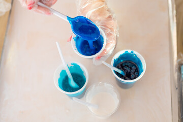 Epoxy resin different blue color in cup for casting stabilizing wood, abstract art. Process of making accessory from resin.Mixing colorful of resin chemical in plastic cup