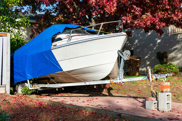 Recreational boat on trailer stored on driveway of residential home. The cruiser is covered with a blue tarp tent for protection. - obrazy, fototapety, plakaty