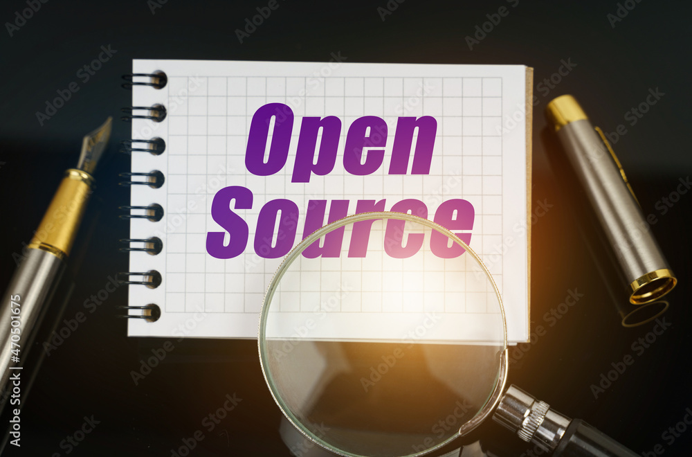 Poster on the black surface is a pen, a magnifying glass and a notebook with the inscription - open source