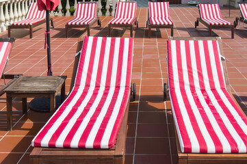 Empty wooden deck chairs with red and white striped mattresses stand in a row. Luxury outdoor...