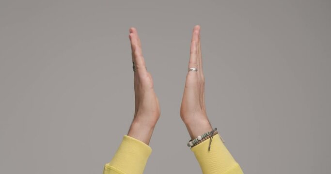 young man's hands with bracelets in the air clapping and celebrating victory in front of grey background in studio