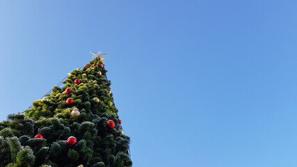 An elegant lonely Christmas tree decorated with garlands and a star against the blue sky. Outdoors, green decorated Christmas tree. As a background and texture for a holiday card with a place for text