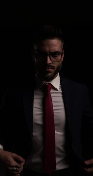 attractive businessman looking down, wearing eyeglasses and buttoning suit, looking to side and walking away in the dark  
