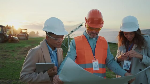 Trio of multi-ethnic male architect and two female engineers wearing helmets safety jacket examing building plan. Cooperation. Plant workers.