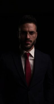 sexy young man with metal frame glasses looking to side, fixing glasses and fading away in the dark