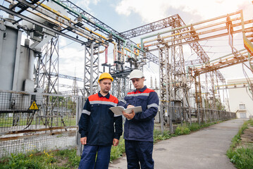 Two specialist electrical substation engineers inspect modern high-voltage equipment in the...