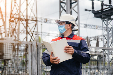 An electrical substation engineer inspects modern high-voltage equipment in a mask at the time of...