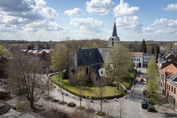 Sint Benedictus church at Mortsel square with blue cloudy sky and trees in autumn. Drone aerial view from above