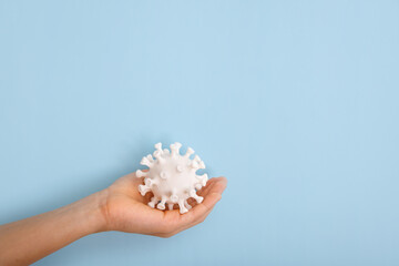 A hand is holding a model of coronovirus on blue background. Coronovirus molecule printed model on a 3D printer.