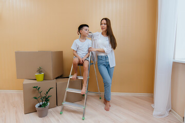 A young woman and her son are standing in front of the boxes and enjoying the housewarming after moving in. Housewarming, delivery and freight transportation, purchase of real estate.