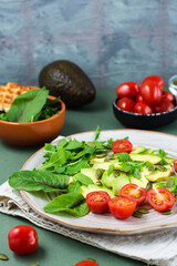 Ready-to-eat salad with avocado, tomatoes, arugula leaves, mizuna, chard and pumpkin seeds on a plate on a green background. Vegetarian vitamin food. Vertical view