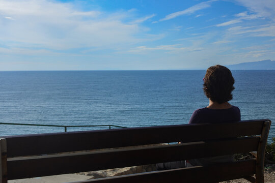 Mujer sentada de espaldas mirando al mar