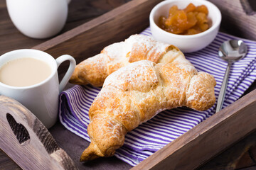 Fresh croissants, jam and a cup of coffee on a wooden tray on the table. Brunch and coffee break