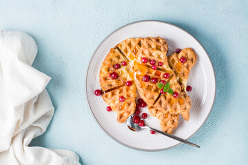Crispy croissant waffles with red currants, honey and mint on plate  on a light table. Sweet mouth-watering breakfast - croffles. Top view