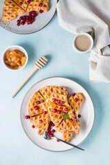 Crispy croffles with red currants, honey and mint on plates, a cup of coffee and jam on a light table. Sweet delicious breakfast. Vertical and top view