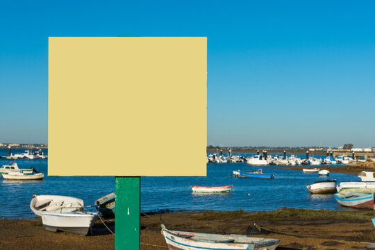 Primer plano de un cartel publicitario, con espacio para copiar, al fondo la playa con barcos de pesca.
