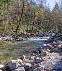 Fototapeta na wymiar Autumn morning on a mountain river, a shallow riverbed with clear water and the rays of the sun illuminating the rocky bottom.