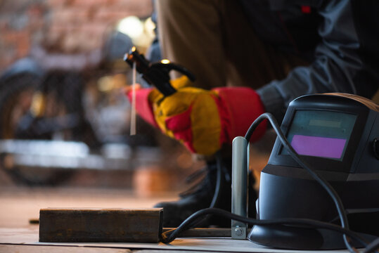 Welder is welding a metal piece close up on the old motorbike background.