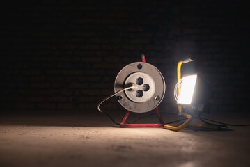 Spotlight lamp and electric power extension cord on the construction site room background.
