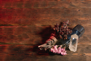 Empty glass bottle and dry herb on the old wooden table background. Witchcraft concept.