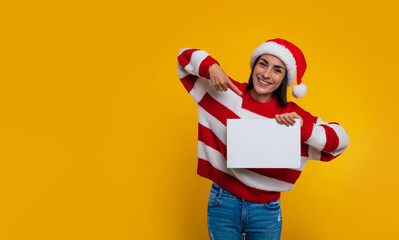 Close up photo of modern charming smiling woman in Christmas stylish clothes while she holds the white blank board in hand and pointing on copy space