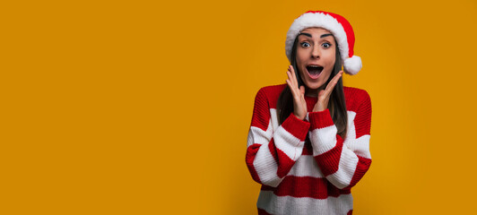 Banner photo of portrait of an excited beautiful young woman in Santa hat in Christmas time while she shouting and having fun on yellow background