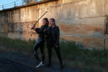 Two warrior women in leather jackets with swords near vintage building