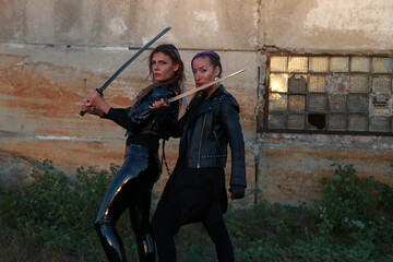 Two warrior women in leather jackets with swords near vintage building