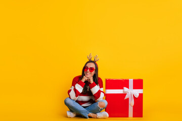 Full length photo of happy young smiling beautiful and charming woman in Christmas reindeer antlers while she sitting with big red gift box