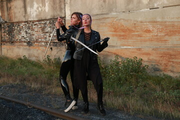Naklejka premium Two warrior women in leather jackets with swords near vintage building