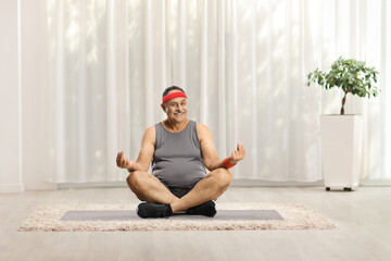 Mature man with a head band sitting on an exercise mat and practicing yoga