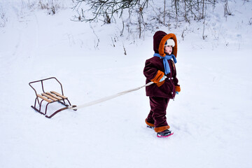 Little child pulling a sled in the snow. The kid is riding on a sleigh. Children play outside in the snow, children ride. Outdoor fun for family Christmas vacations.