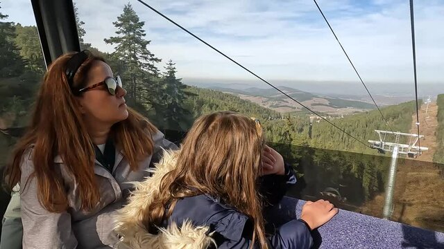 Mother and daughter driving with aerial lift, view Autumn nature landscape from cable car.