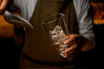 close-up of clear glass in bartender hand with ice cubes into it