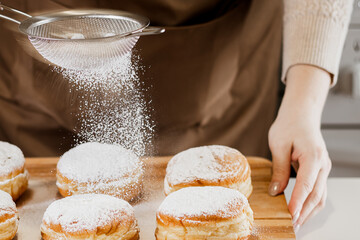 Woman prepares fresh donuts with jam in home kitchen. Cooking traditional Jewish Hanukkah sufganiyot.