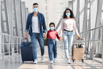 Fototapeta na wymiar Middle-Eastern Family Of Three Wearing Medical Masks Walking With Luggage In Airport
