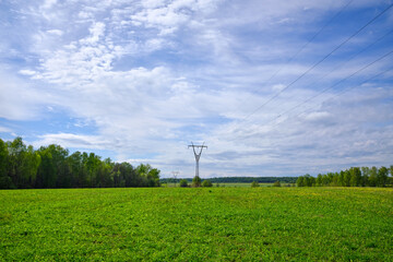Fototapeta na wymiar High voltage power lines through fields against a blue sky with clouds on a summer day.