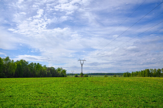 High voltage power lines through fields against a blue sky with clouds on a summer day.