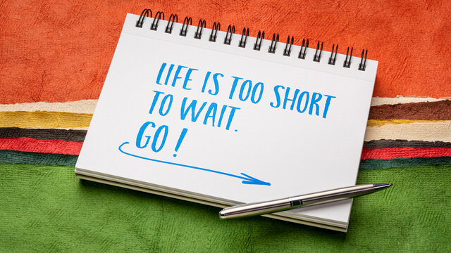 Life is too short to wait. GO! Inspirational handwriting in a sketchbook against abstract paper landscape.