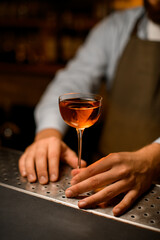 beautiful wine glass with alcoholic drink on steel bar surface and male hand holds it.