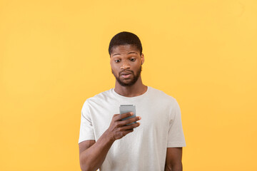 Emotional african american guy looking at smartphone, reading shocked message of promo or offer, yellow background