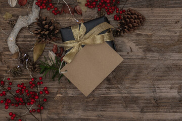 blank christmas card with space to write on a gift on a wooden surface decorated with pine cones, berries and led lights