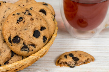 Chocolate cookies in a basket on the background of a glass cup of tea. Close-up.