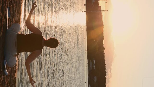 vertical video. a man sits in a lotus position. on the shore at sunset. isoteric theme. High quality 4k footage