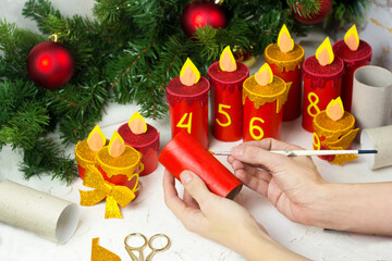 Woman making handmade advent calendar with toilet paper tubes at home. Girl Coloring rolls. Christmas candle craft.