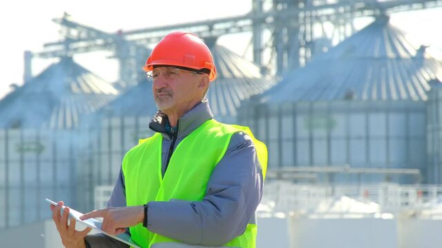 Grain elevator marine shipping. Senior taskmaster inspects new silo making marks online on tablet computer in modern docks