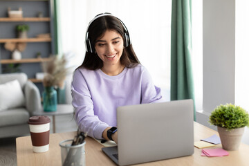 Smiling woman using computer, wearing wireless headphones